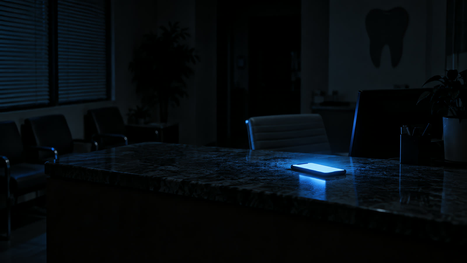 Recepción de una clínica dental de noche, a oscuras, con un celular encendido sobre el mesón.
